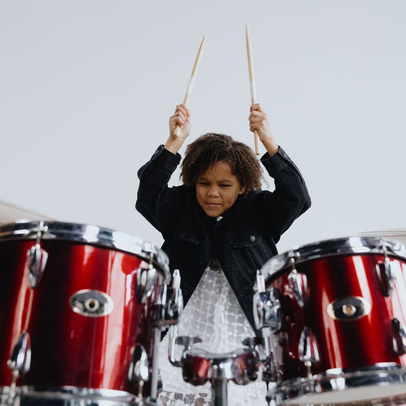 A young drummer raising the sticks over a red drum kit