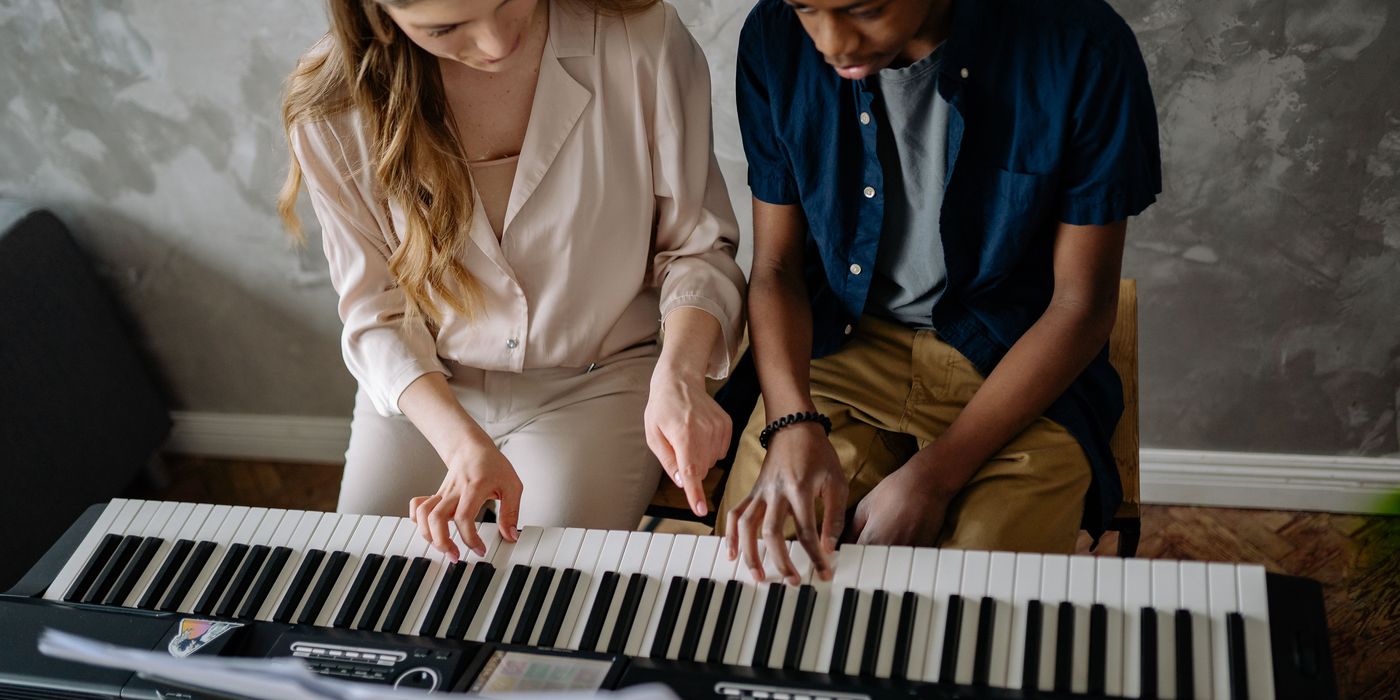 A tutor and a student playing a keyboard side by side